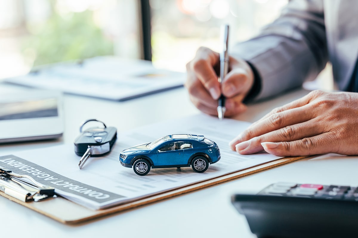 Homme signant un contrat d'assurance auto avec des clés de voiture sur la table