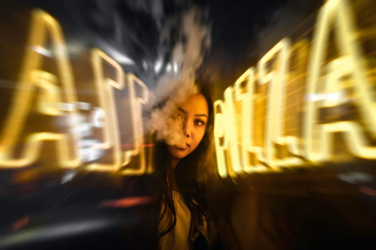 Femme près d'un panneau néon jaune en train de vapoter
